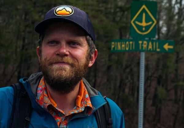 Professor Carl smiles infront of a Pinhoti Trail sign