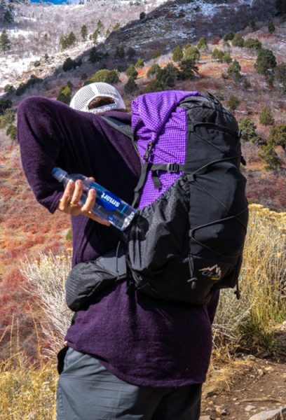 A backpacker inserts his water bottle into the side pocket of a frameless CDT backpack.