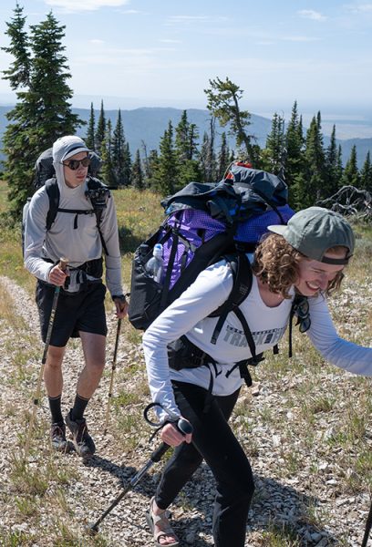 Two backpackers hike up a trail towards the camera. The front backpacker is smiling.