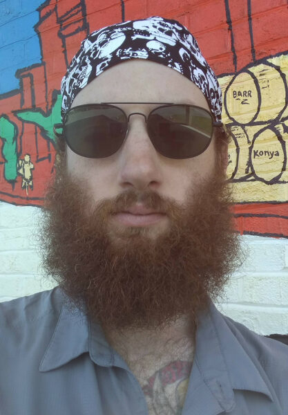 A bearded man wears a due rag and sunglasses. Would you pick up this man?