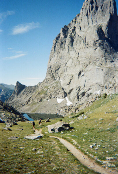 An alpine lake on Cirque of the Towers. A hiking trail is shown leading into a lake with a rock face behind it.