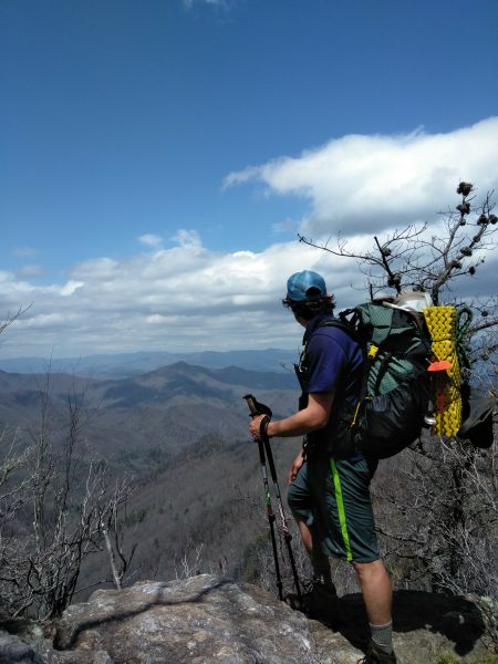 A man stares out over an overlook. he is wearing a green ULA backpack.