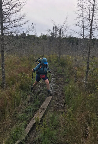 A female backpacker jumps over the mud and onto a piece of board