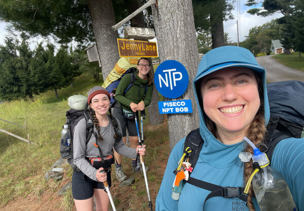 Three women with backpacks smile in front of the Northville Placid Sign