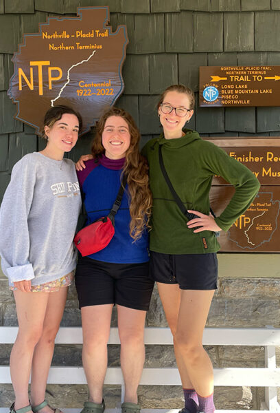 Three Women Smile in front of the northville placid trail sign
