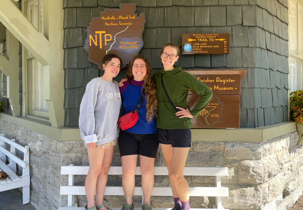 Three women smile and pose infront of the Northville Placid Trail sign