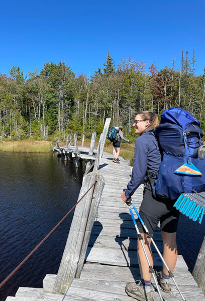 Woman looks out at a like while backpacking across a wooden bridge.