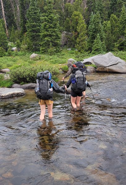 Three hikers cross a calf deep river crossing