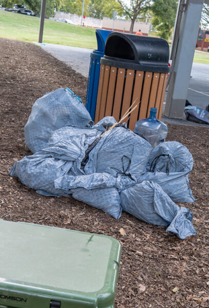 A pile of trash bags next to a trash can after a park clean up