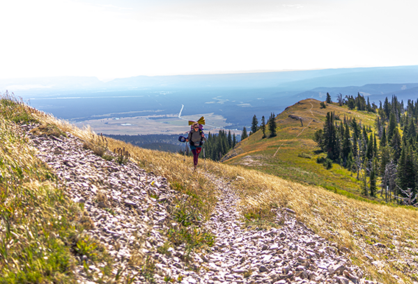 Amelia hikes up a mountain. There is a beautiful vista behind her.