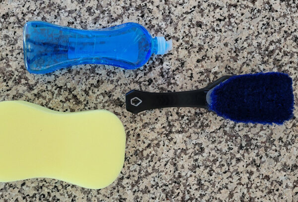 A soft brush, sponge, and dish soap sit on a counter, ready to clean a ULA pack