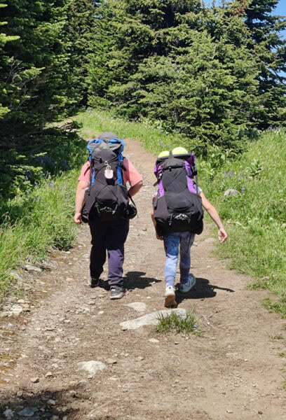 A boy and girl wearing ULA kids packs race up the trail