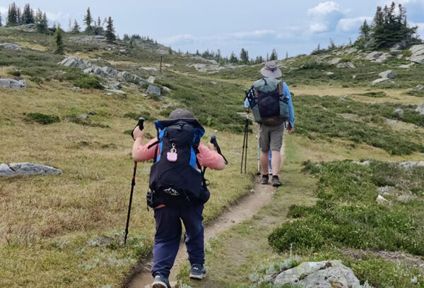 A boy wearing a ULA Kids Spark follows his uncle wearing a ULA Catalyst up the trail