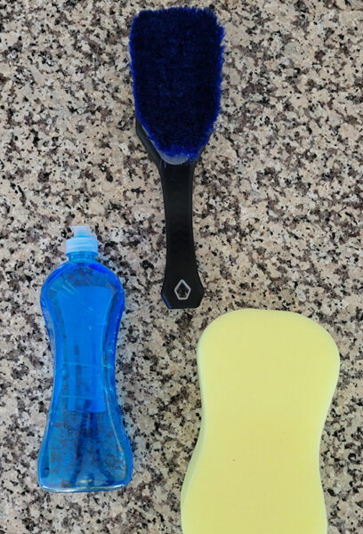 A soft brush, sponge, and dish soap sit on a counter, ready to clean a ULA pack