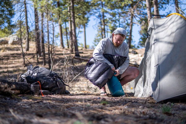 A backpacker crams his sleeping bag back into its stuff sack outside his tent