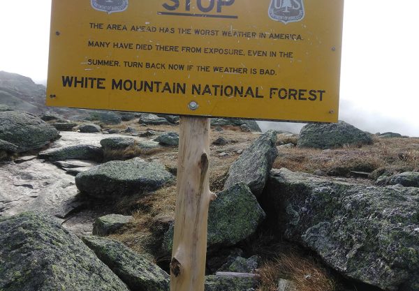 A bright yellow warning sign on the Appalachian trail warning of the worst weather in America and risk of death by exposure in the White Mountain National Forest.