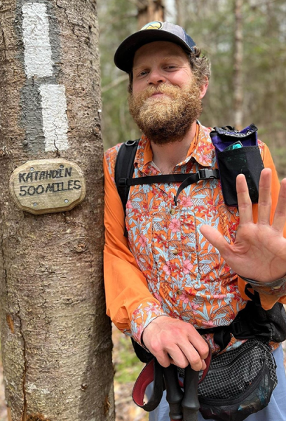 Professor Carl waves at the camera next to the tree with the "Katahdin 500 mile" sign.