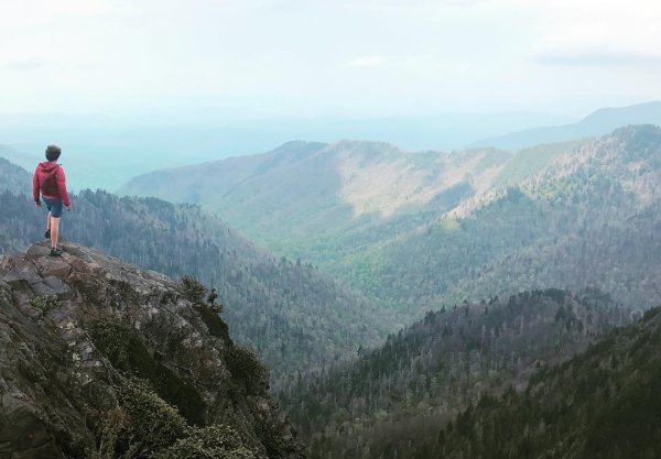 A hiker stands on a cliff's edge, a huge view of Appalachia stretched out before them.