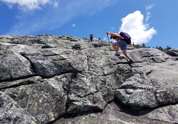 Through hikers hand-over-footing up the side of a rockface on the Appalachian Trail.