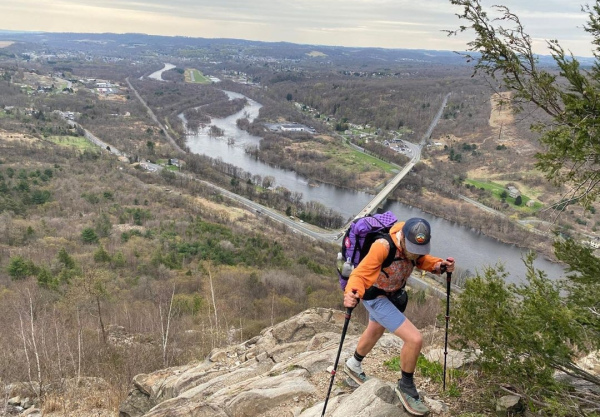 Through hiker Profesor Carl hiking up a hillside on the Appalachian Trail. There is a town and river in the background.