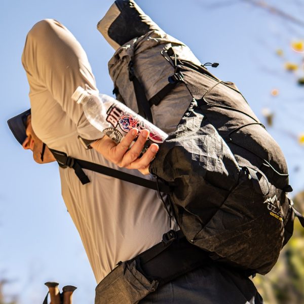 A hiker reaches for their water bottle in the angled side pocket of the ULTRA Circuit SV
