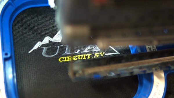 An upclose image of the embroidery machine's needle finishing the logo and "Circuit SV" stitching on a pack.