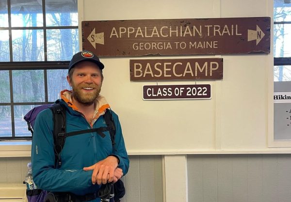Through hiker Professor Carl stands next to an Appalachian Trail sign at basecamp.