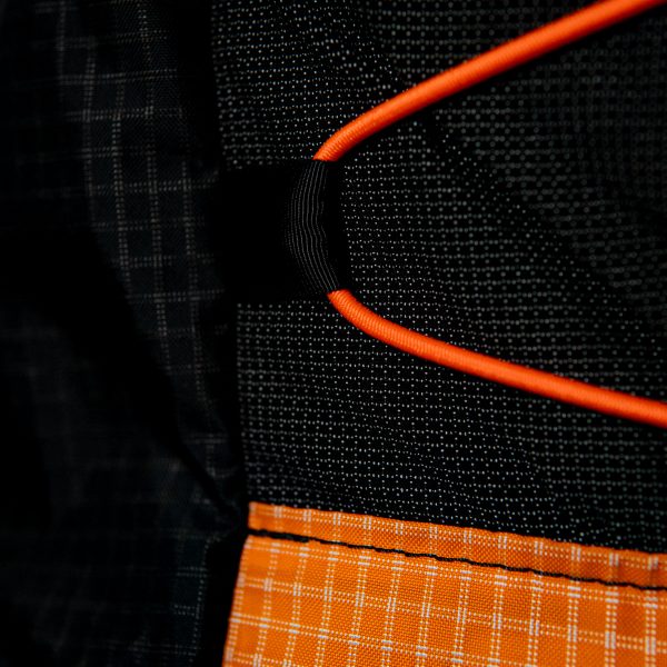 A close up of the front cinch cord holders on a Tangerine colored UltraGrid Nexus. The cinch cord is bright orange like the pack.