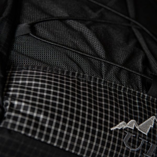 A close up of the bottom of a Nexus pack in Black Beauty UltraGrid. It shows where the bottom pannel and UltraStretch Mesh front pocket meet.
