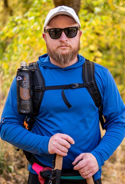 A hiker in a blue shirt faces the camera; his shoulder straps fit correctly, and his sternum strap is in the correct possition across his chest.