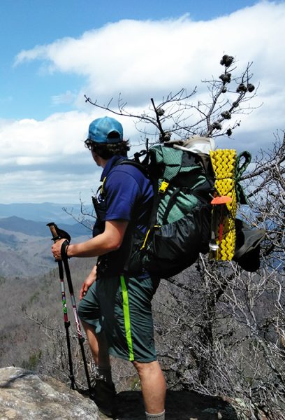 A Hiker stands on a mountain top on a gear shakedown trip. He has a yellow foam sleeping pad strapped to the outside of his pack.