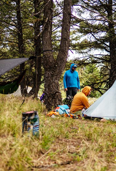Two hikers set up their ultralight shelters in the Montana Wilderness. There is a bear bin in the foreground.