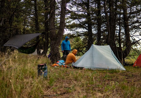 Two hikers set up their ultralight shelters in the Montana Wilderness. There is a bear bin in the foreground.