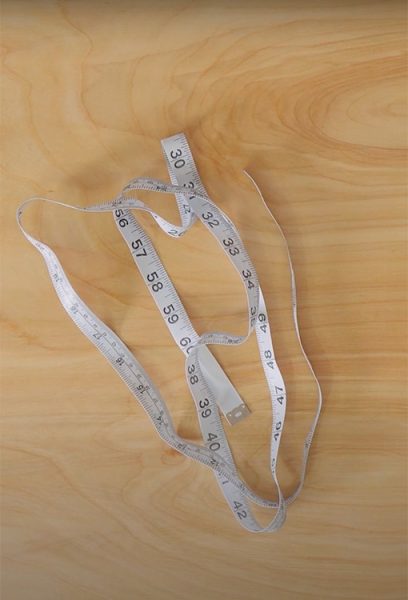 A measuring tape sits on a wood table top[.