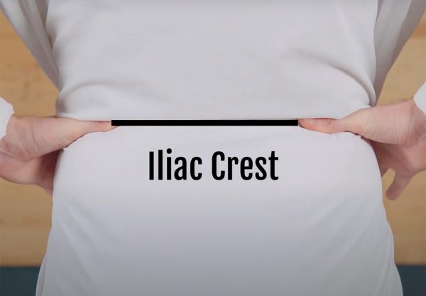 A hiker points to their iliac crest. Their hands are around their waist at the top of their hip bone.