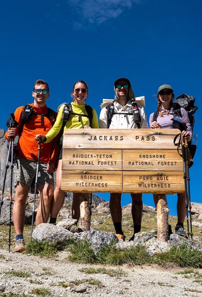 Four backpackers stand infront of a sign for Jackass Pass dividing the Bridger-Teton National Forest and the Shoshone National Forest in Wyoming