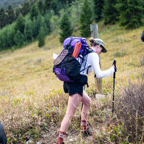 A female hiker hikes up a hill wearing a purple robic ULA Catalyst.