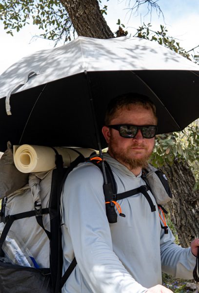A backpacker tests his UV umbrella and a ULA foam pad.
