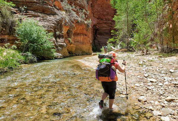 A through hiker crosses a shallow creek in the canyonlands of Utah.