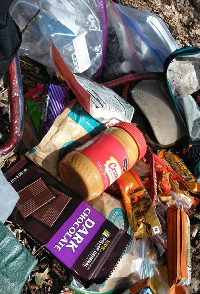 A hiker's resupply sits on the ground it contains items like peanut butter and chocolate