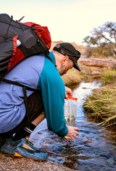 A hiker fills his water filter bag from a stream.