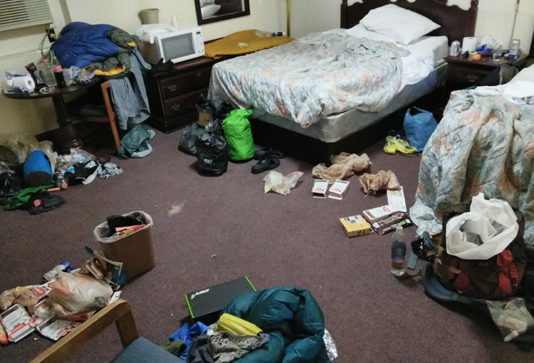 thru-hikers share a hotel room on the AT Backpacker reaches for his bear spray from the ULA Deploy Bear Canister Holder on his shoulder strap.