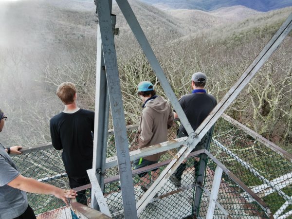 Three hikers standing on some sort of metal overlook; maybe a fire lookout. Image is blurry