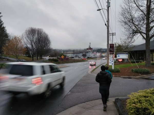 Two hikers walking down a sidewalk in a trail town. It is cloudy and raining.
