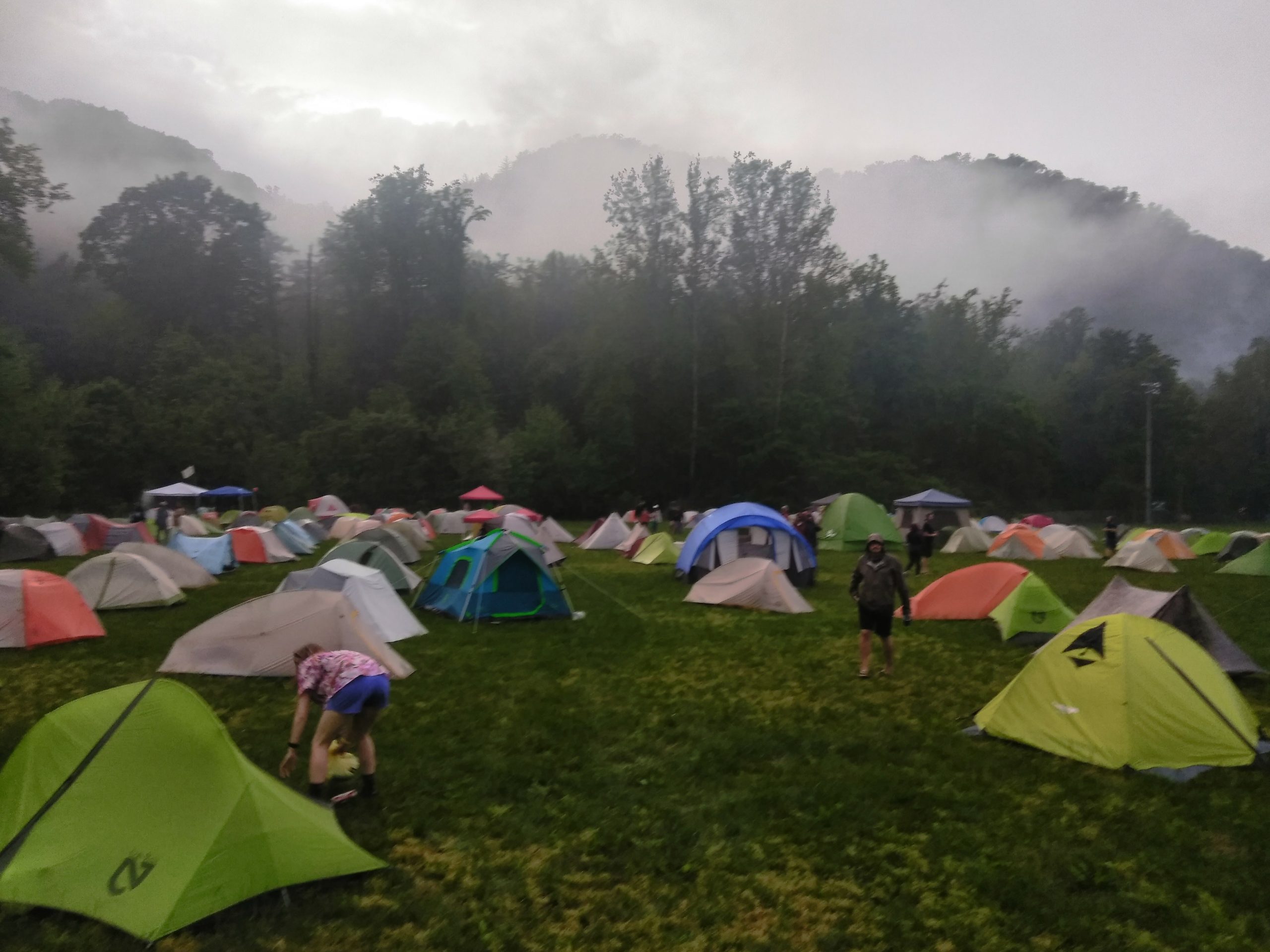 Dozens of tents and campers set up in a large field. It is very foggy and cold looking.