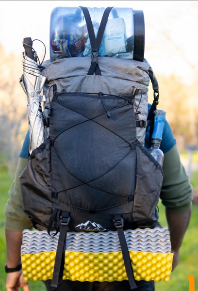 A backpacker using the top Y-strap to hold down his bear bin on the outside of his pack, and the bottom straps to carry his sleeping pad.
