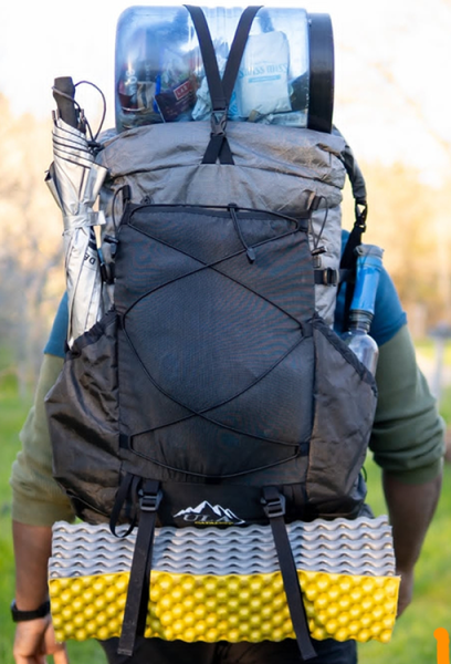 A backpacker using the top Y-strap to hold down his bear bin on the outside of his pack, and the bottom straps to carry his sleeping pad.