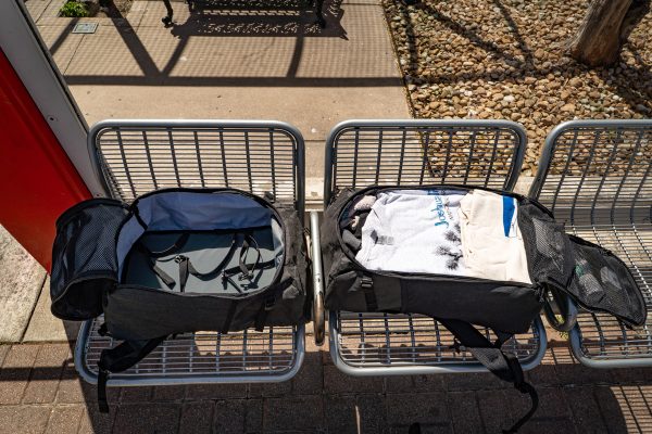 An empty 30L Dragonfly is open on a bus stop bench. A 36L is open next to it and is fully packed. You can see the internal compression straps.