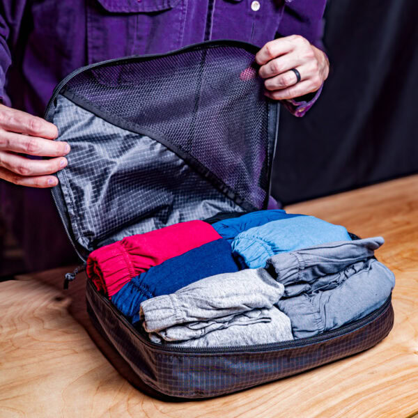 A traveler folds 6 pair of underwear/shorts in a large packing cube.