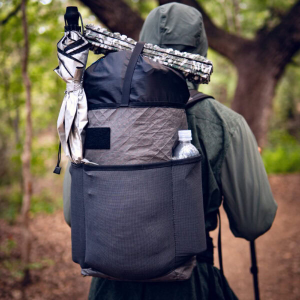 An Ultralight hiker goes backpacking with a Packrat pack. They have their sleeping pad strapped to the top, and a UV umbrella in the side mesh pocket.